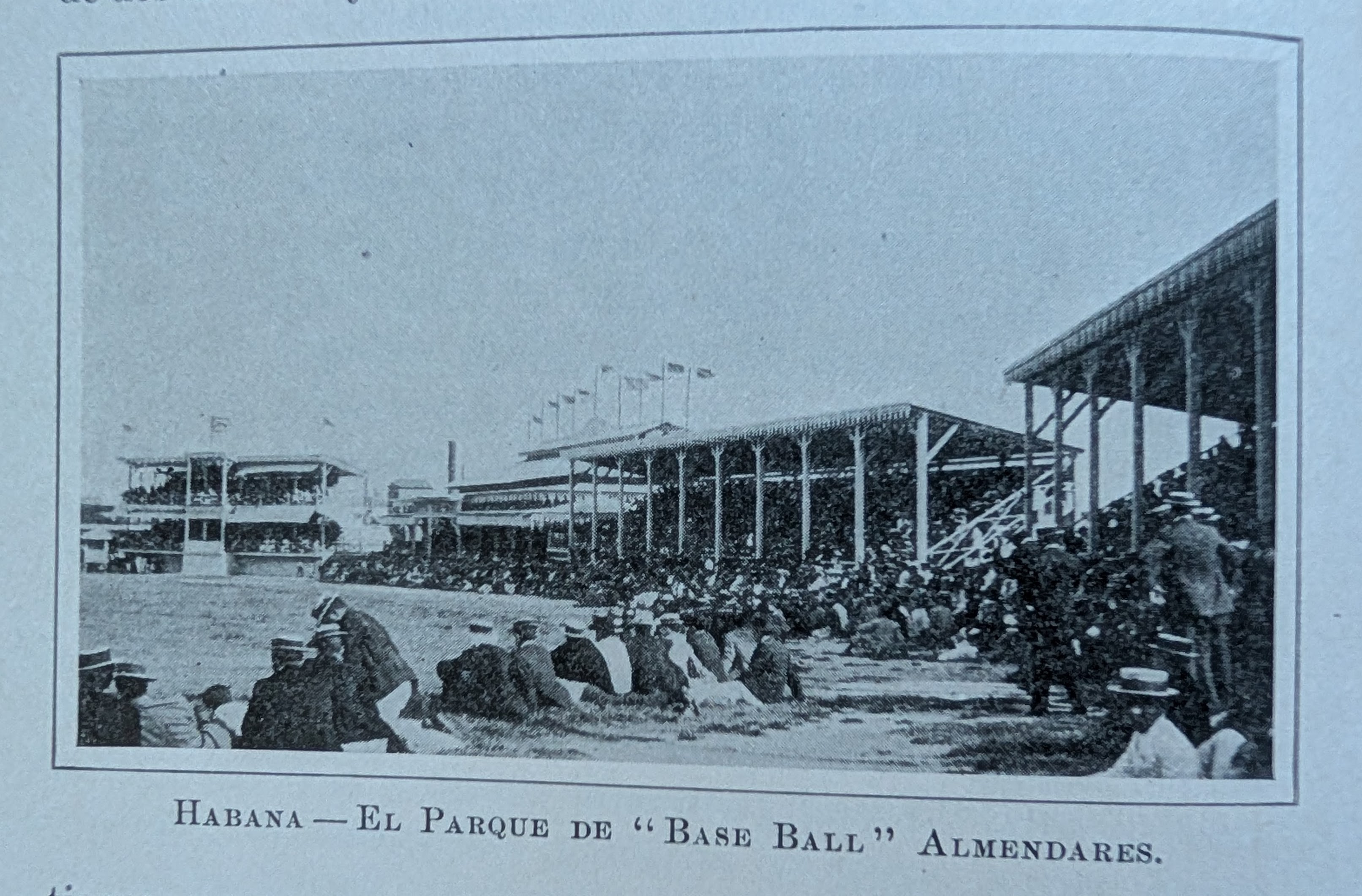Antique photo of men in boater hats sit on the ground and in bleachers at a open-field stadium. The caption, in Spanish, reads, Habana, The Almendares baseball park.