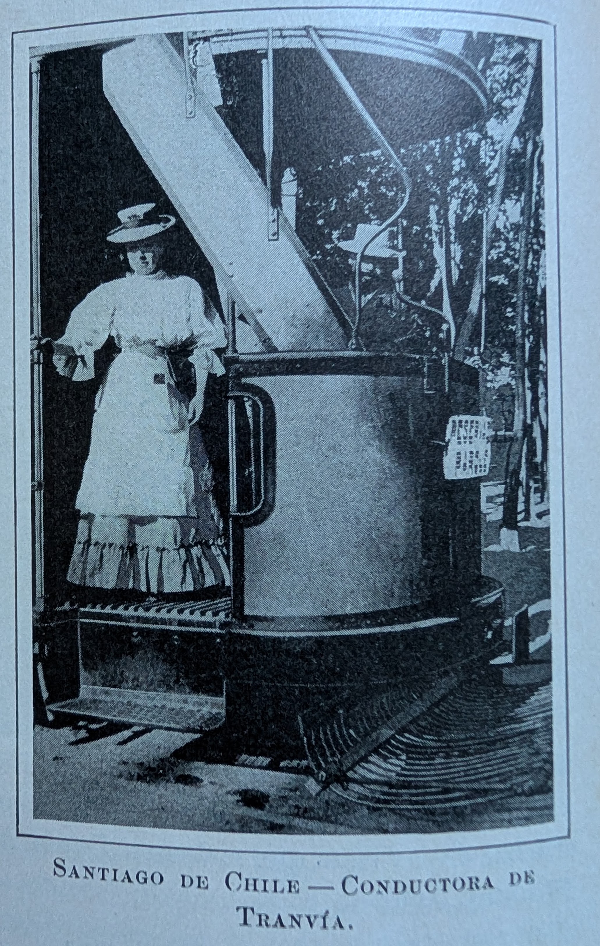 Antique photo showing a woman tram conductor, wearing a dress and boat hat, standing at the back of a tram. The caption, in Spanish, reads, Santiago in Chile, tram conductor.