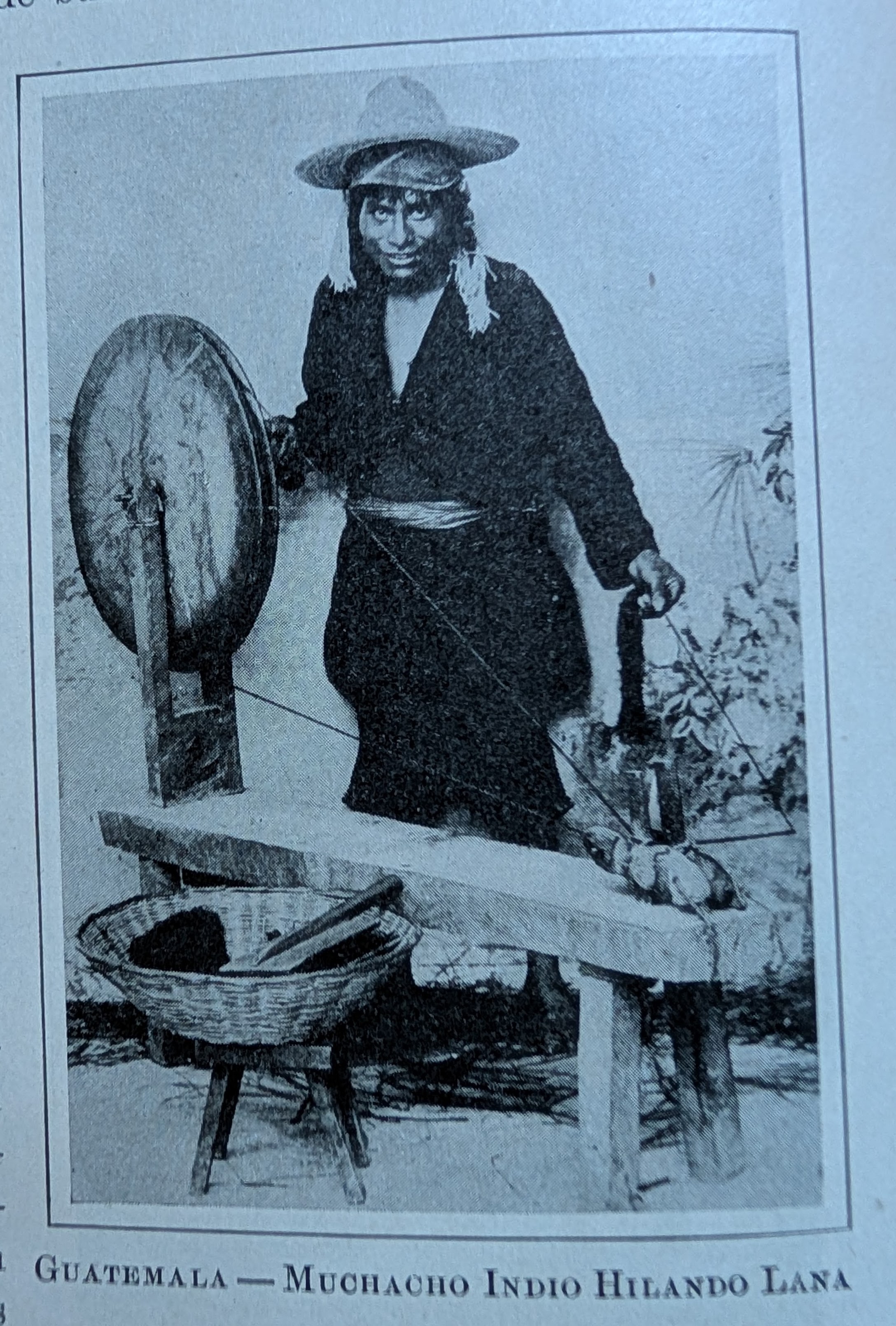 Antique photo showing a young indigenous man spinning thread on a spinning wheel. The caption, in Spanish, reads, Guatemala, Indian boy spinning wool.