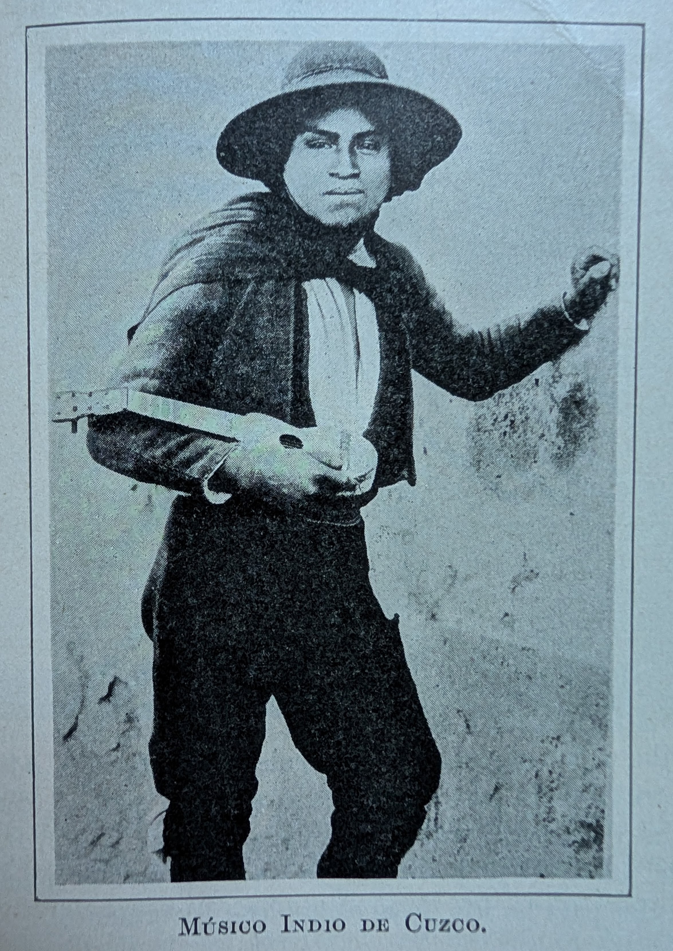 Antique photo showing a young man in a hat posing against a wall with a charango in one arm. The caption, in Spanish, reads, Indian musician from Cuzco.